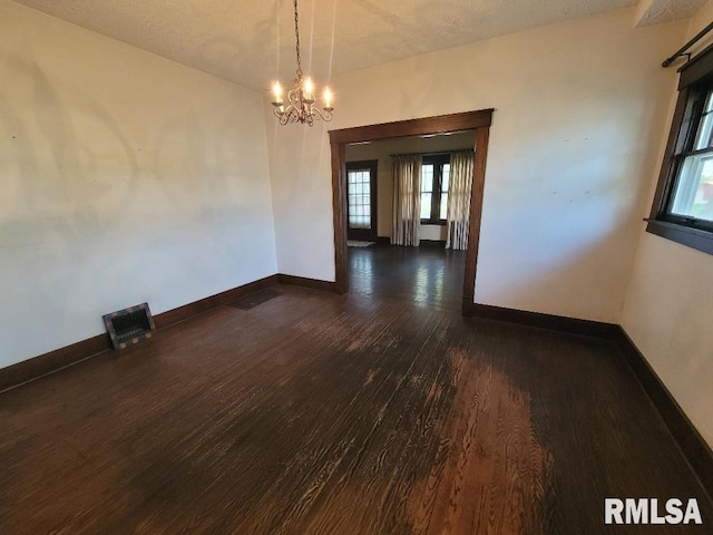 empty room with dark wood-type flooring, visible vents, baseboards, and a notable chandelier