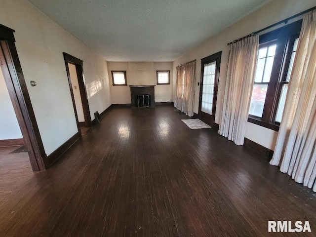 unfurnished living room featuring a fireplace, baseboards, and dark wood-type flooring
