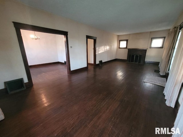 unfurnished living room with dark wood-style floors, an inviting chandelier, visible vents, baseboards, and a fireplace