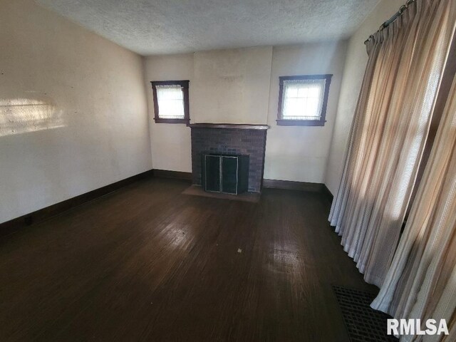 unfurnished living room with dark wood finished floors, plenty of natural light, a textured ceiling, and baseboards
