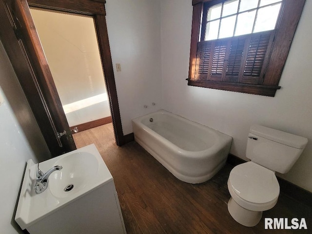 bathroom featuring a bath, wood finished floors, toilet, and a sink