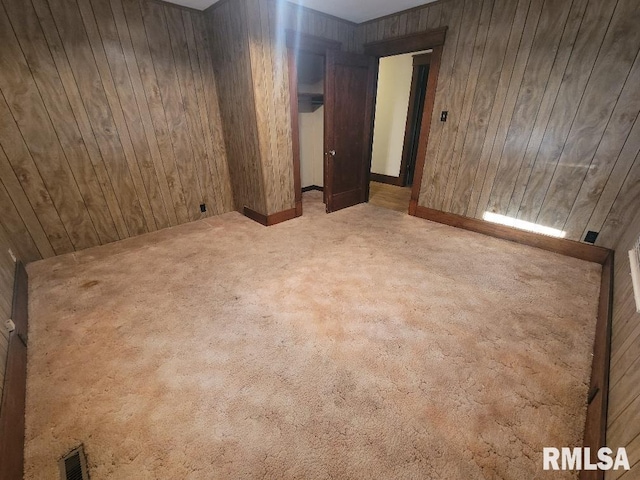 carpeted empty room featuring wood walls and visible vents