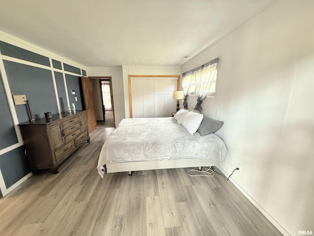 bedroom with wood finished floors, baseboards, visible vents, and a closet