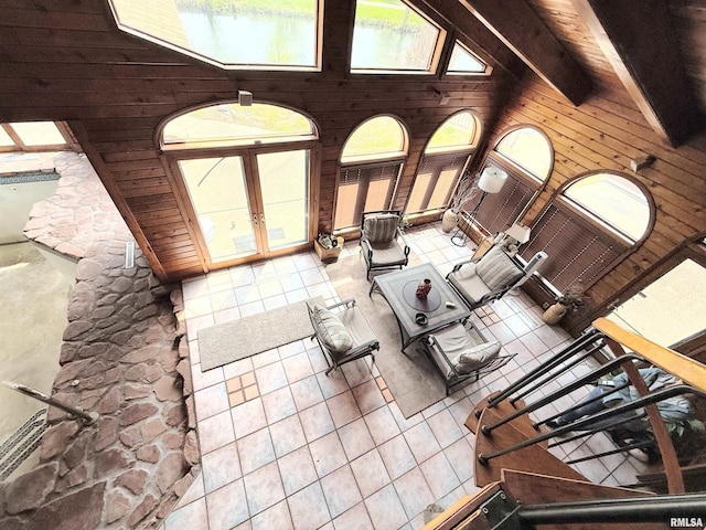 unfurnished living room featuring high vaulted ceiling, a healthy amount of sunlight, tile patterned flooring, and wooden walls