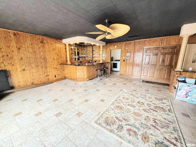 unfurnished living room with a ceiling fan, a bar, wooden walls, washer / clothes dryer, and ornate columns