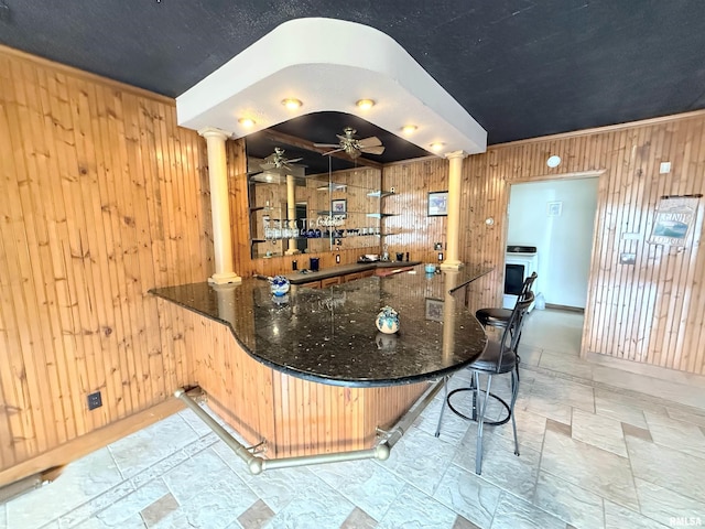 bar featuring wood walls, a ceiling fan, and decorative columns