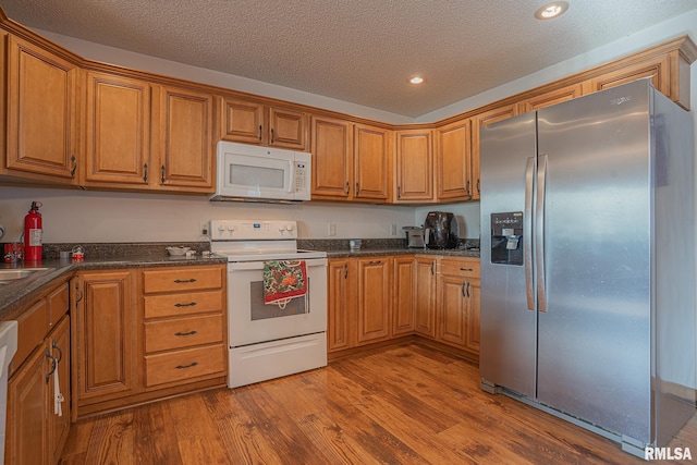kitchen with brown cabinetry, a textured ceiling, wood finished floors, and white appliances