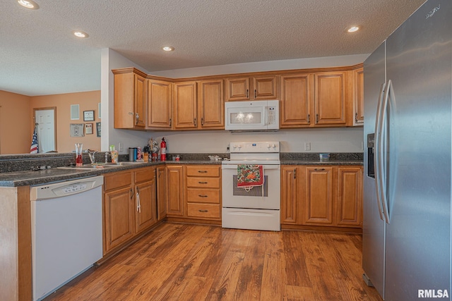 kitchen with a textured ceiling, dark countertops, wood finished floors, white appliances, and brown cabinetry