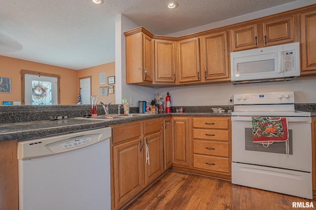kitchen with dark countertops, wood finished floors, white appliances, and brown cabinets