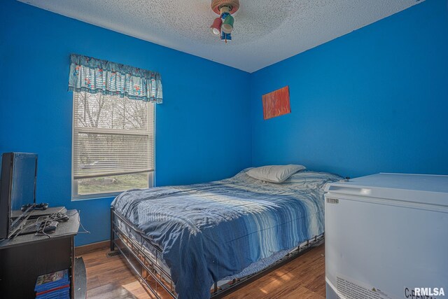 bedroom with refrigerator, ceiling fan, a textured ceiling, and wood finished floors