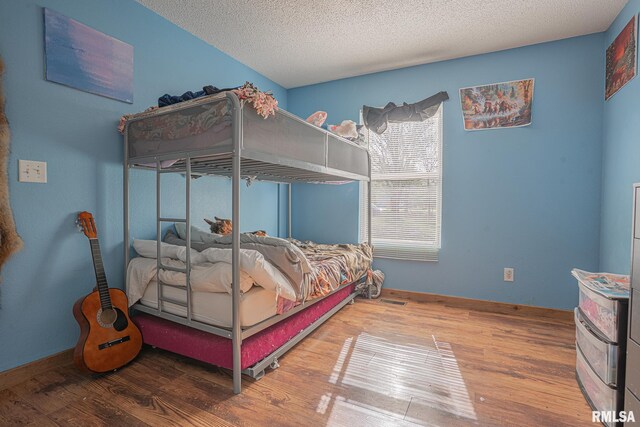 bedroom featuring baseboards, wood finished floors, and a textured ceiling