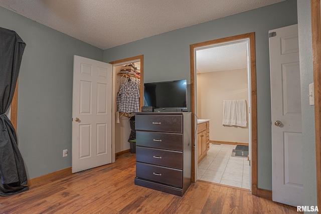 bedroom featuring light wood finished floors, a closet, a walk in closet, and a textured ceiling