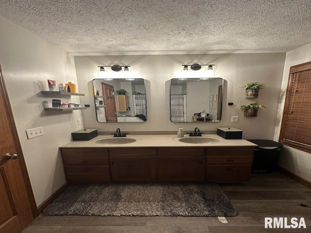 full bathroom with wood finished floors, a textured ceiling, double vanity, and a sink