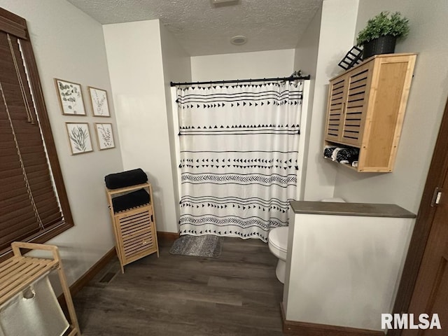 full bath featuring toilet, baseboards, a textured ceiling, wood finished floors, and a shower with shower curtain