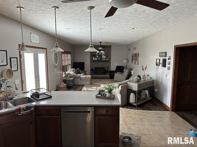 kitchen featuring pendant lighting, stainless steel dishwasher, a sink, ceiling fan, and a fireplace