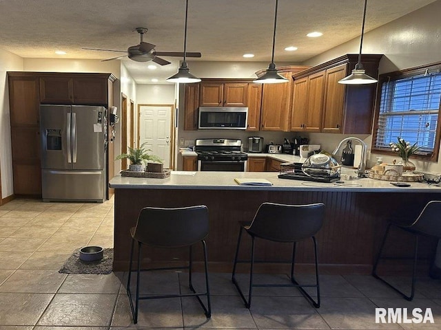 kitchen with ceiling fan, a breakfast bar, decorative light fixtures, a peninsula, and appliances with stainless steel finishes