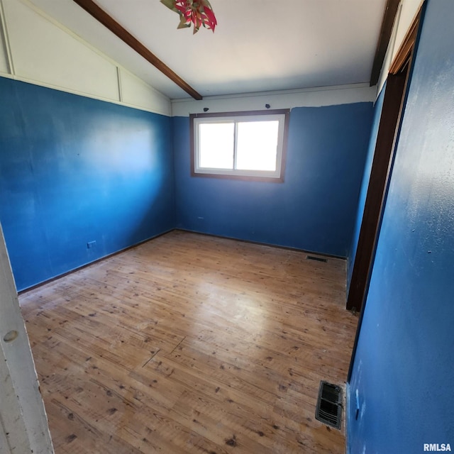 empty room with visible vents, vaulted ceiling with beams, and wood finished floors