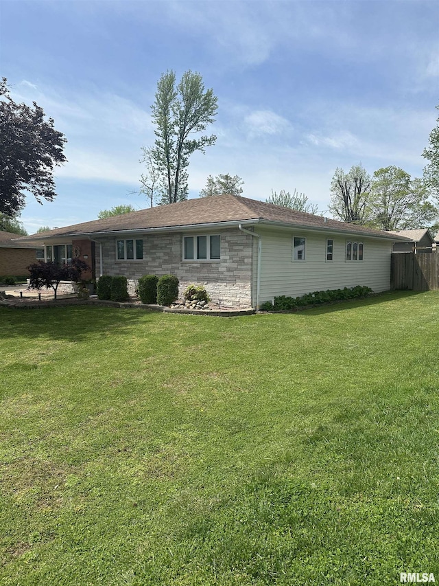 back of house featuring a yard, stone siding, and fence
