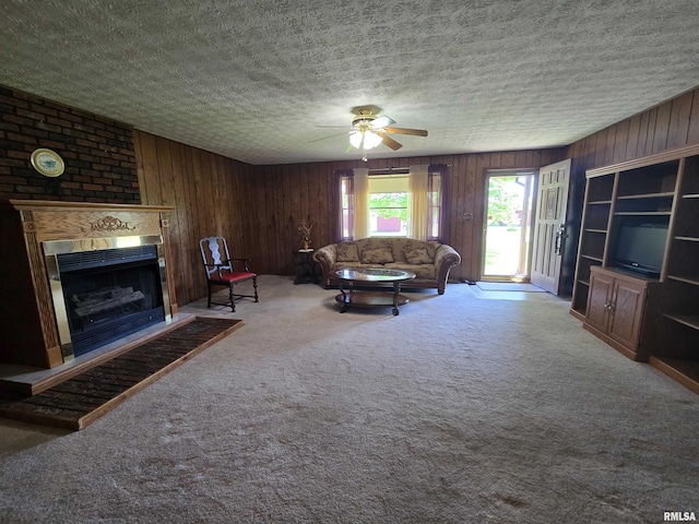 carpeted living room featuring a fireplace, a ceiling fan, wood walls, and a textured ceiling