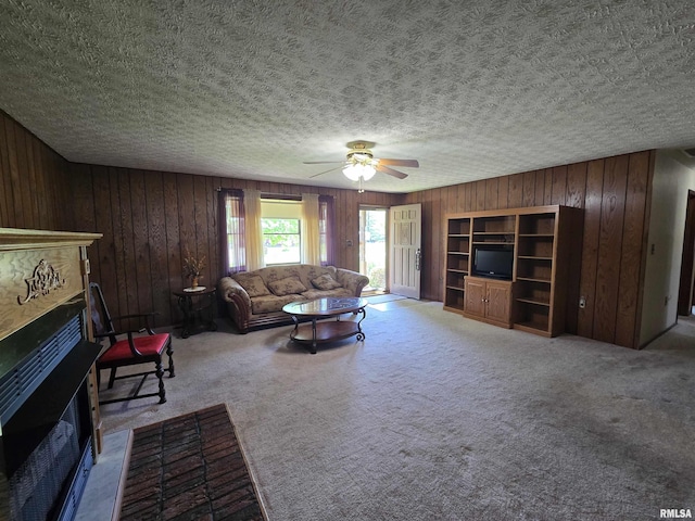 living area with a fireplace, carpet floors, a textured ceiling, wood walls, and a ceiling fan