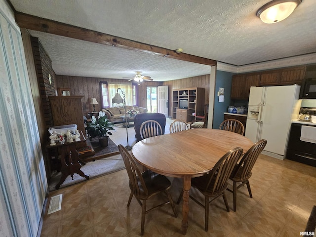 dining room with beam ceiling, a textured ceiling, wood walls, a ceiling fan, and visible vents
