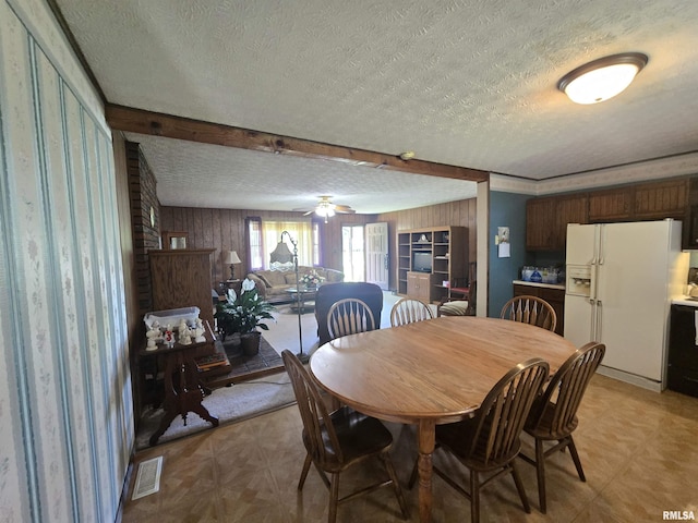 dining space with light floors, a textured ceiling, wooden walls, and visible vents