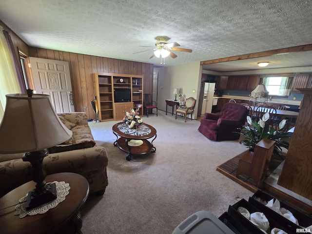 carpeted living area with ceiling fan, wood walls, and a textured ceiling
