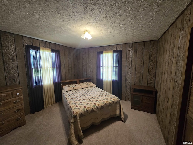 bedroom with wooden walls, a textured ceiling, and light carpet