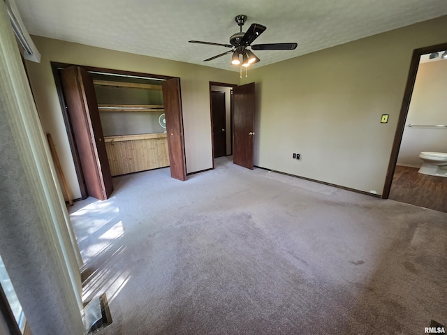 unfurnished bedroom with baseboards, multiple closets, light carpet, and ceiling fan