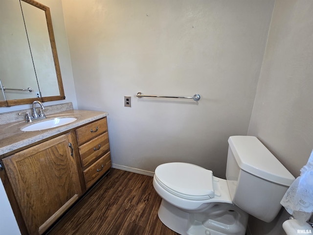 half bath featuring vanity, baseboards, toilet, and wood finished floors