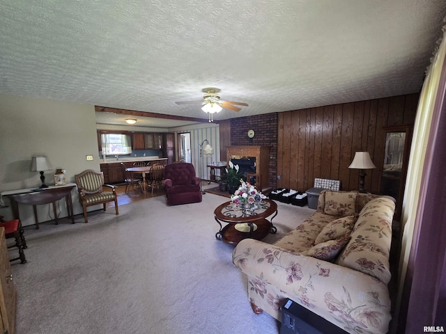 living area with ceiling fan, carpet, a brick fireplace, and a textured ceiling