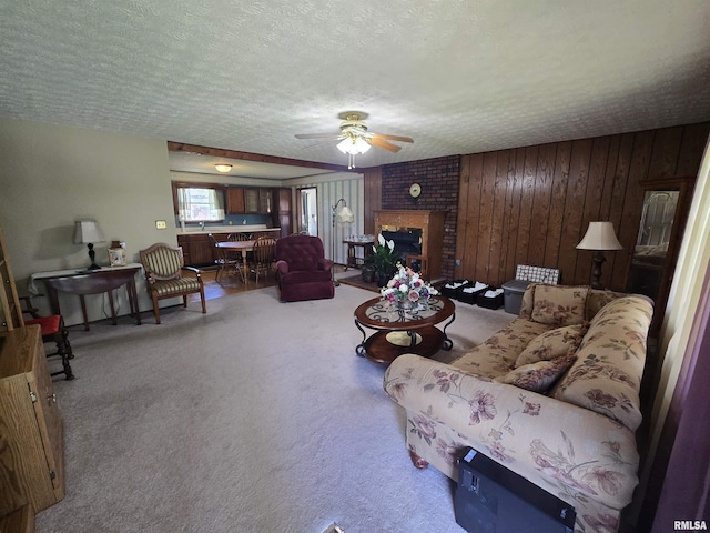 living room featuring ceiling fan, a brick fireplace, carpet flooring, and a textured ceiling