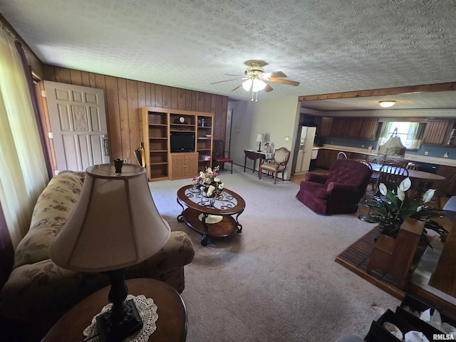 living area with a textured ceiling, carpet, a ceiling fan, and wooden walls