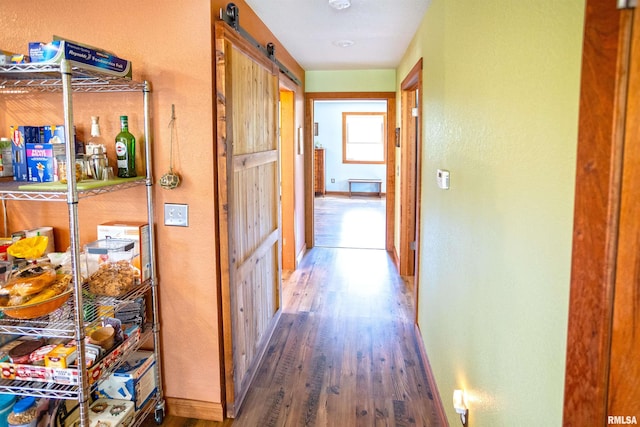 corridor featuring wood finished floors, baseboards, and a barn door
