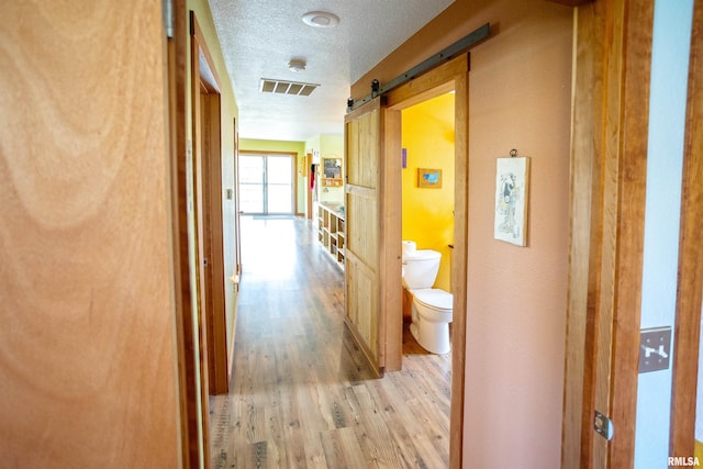 hallway with a textured ceiling, visible vents, light wood finished floors, and a barn door