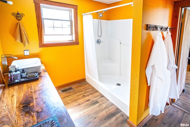 bathroom featuring visible vents, wood finished floors, a shower stall, and a sink