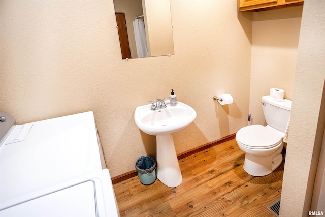 bathroom with a sink, washer / dryer, toilet, baseboards, and wood finished floors