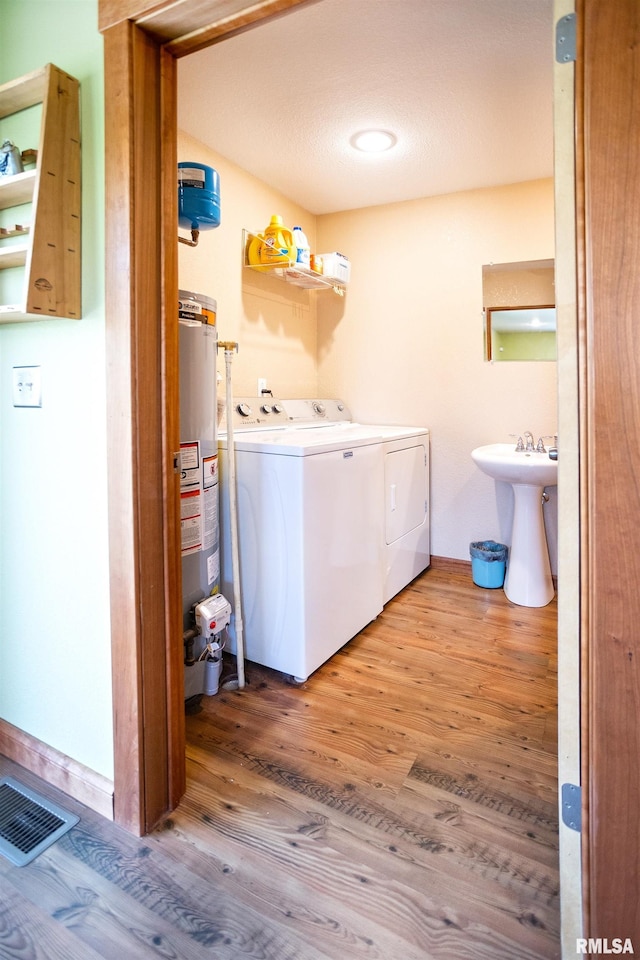 laundry area with gas water heater, washing machine and clothes dryer, laundry area, visible vents, and light wood-style flooring