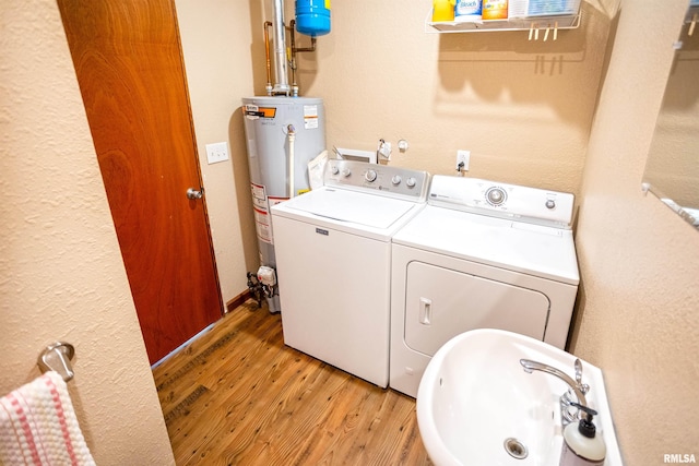laundry area featuring separate washer and dryer, a sink, water heater, and light wood-style floors