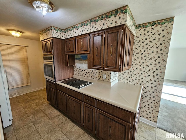 kitchen with freestanding refrigerator, dark brown cabinetry, oven, light countertops, and black electric cooktop