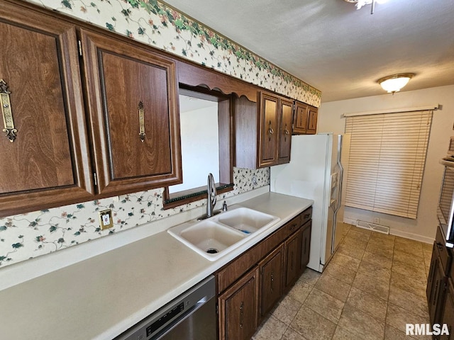 kitchen featuring dark brown cabinetry, white refrigerator with ice dispenser, a sink, light countertops, and visible vents