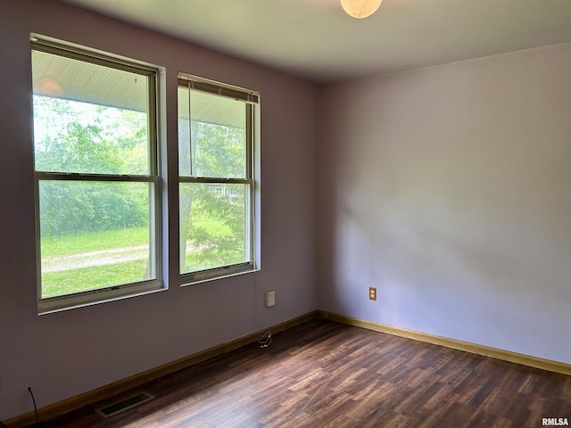 unfurnished room with visible vents, dark wood finished floors, and baseboards