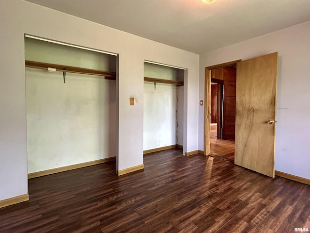 unfurnished bedroom with baseboards, two closets, and dark wood finished floors
