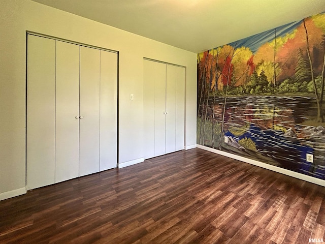 unfurnished bedroom featuring multiple closets, baseboards, and wood finished floors