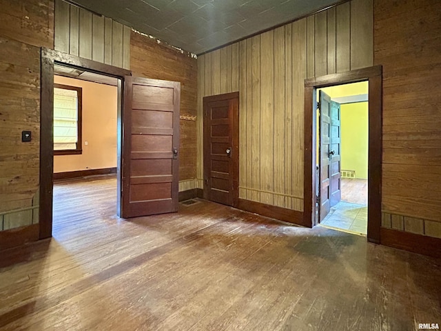 spare room with wooden walls, baseboards, wood finished floors, and visible vents