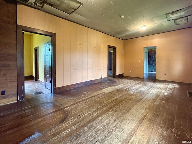 spare room with wood-type flooring, wood walls, and visible vents