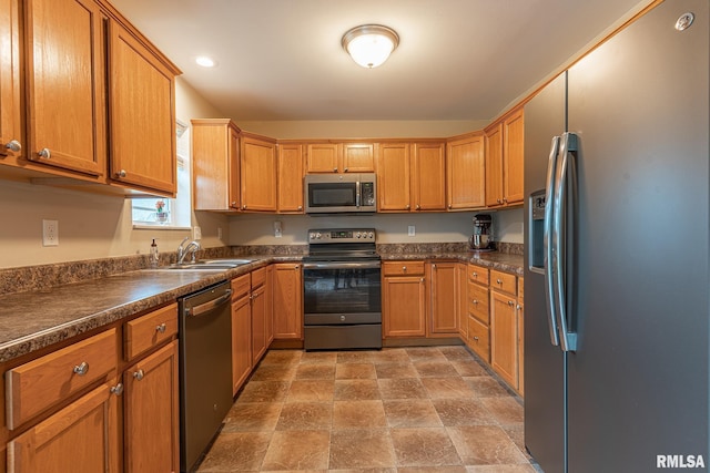 kitchen featuring stone finish floor, appliances with stainless steel finishes, dark countertops, brown cabinets, and a sink