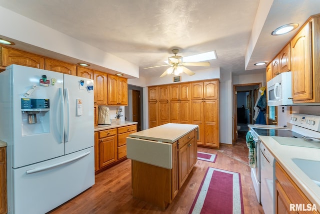 kitchen with a kitchen island, a ceiling fan, wood finished floors, light countertops, and white appliances