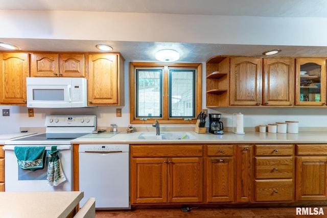 kitchen with white appliances, brown cabinetry, a sink, and light countertops