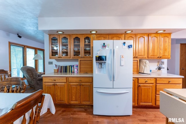 kitchen featuring light wood-type flooring, light countertops, white refrigerator with ice dispenser, and glass insert cabinets